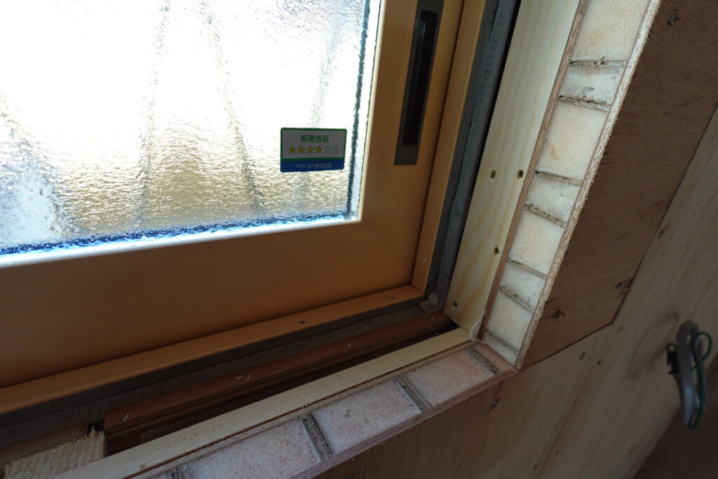 キッチンガラス2 | みすずのリフォーム |四日市市の断熱リノベーション・性能向上リフォーム Frosted window pane with a green/blue energy rating sticker on a wooden frame in a building under construction.